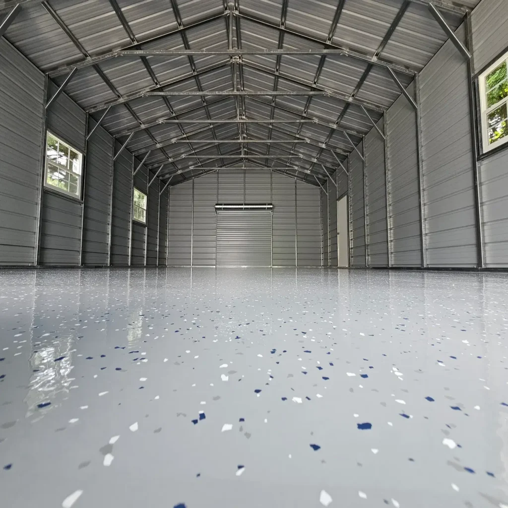 Epoxy garage flooring with gray flake finish, glossy seamless surface, and spacious metal garage interior with high ceilings.